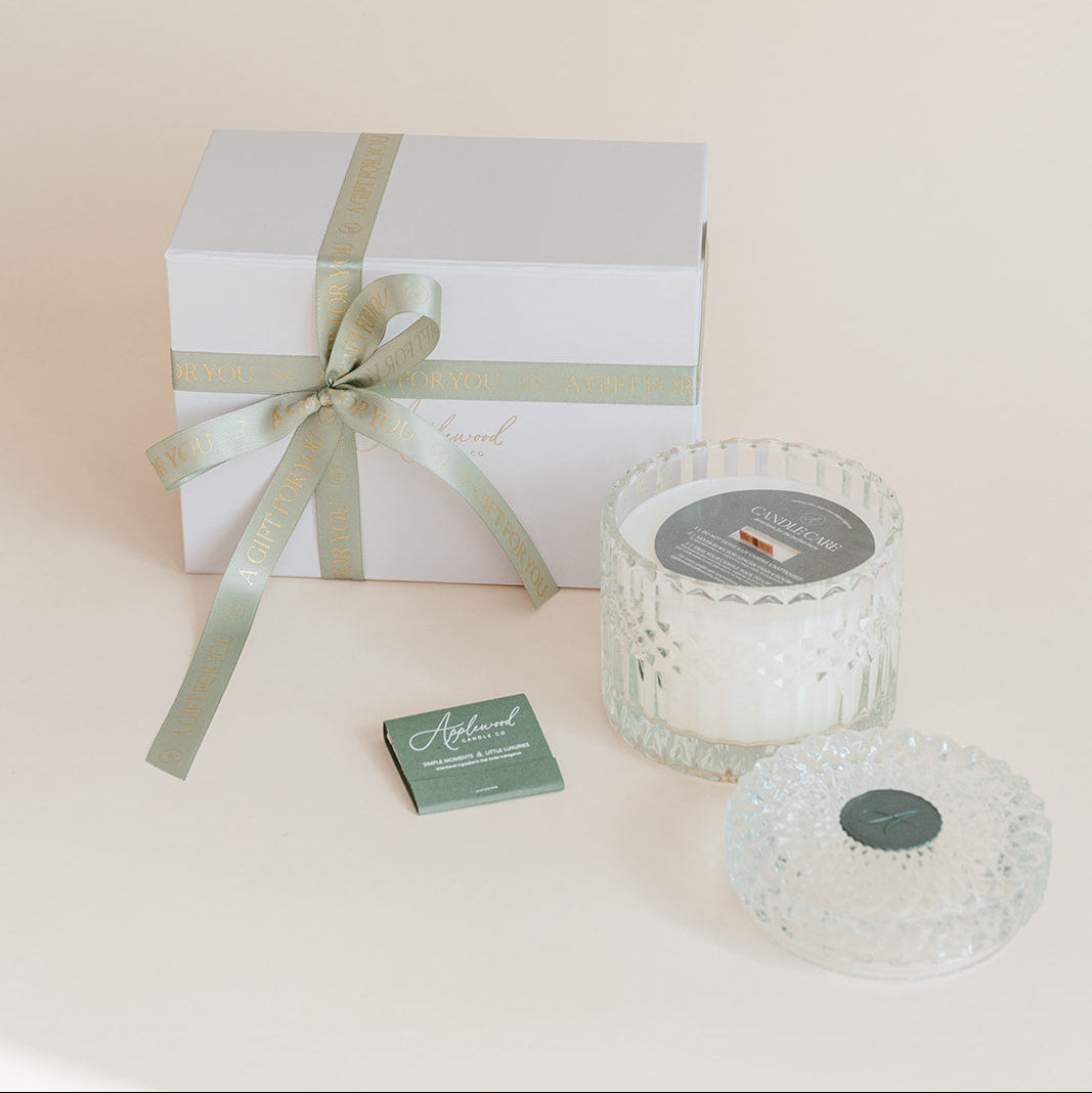 Gift box with a ribbon, two glass candle holders, and a card on a light background