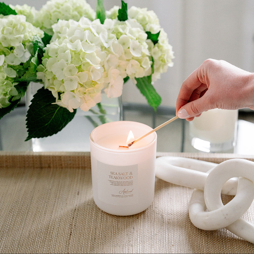 Sea Salt & Teakwood Candle in glass frosted jar being lit.