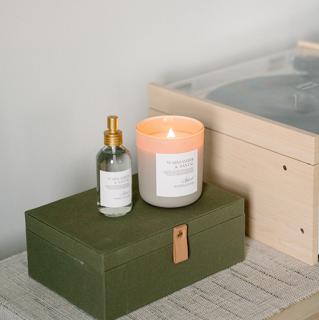 Warm Amber & Santal frosted glass candle and room & linen mist on green box.