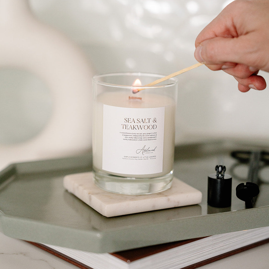 Sea Salt & Teakwood Candle in clear glass jar being lit.