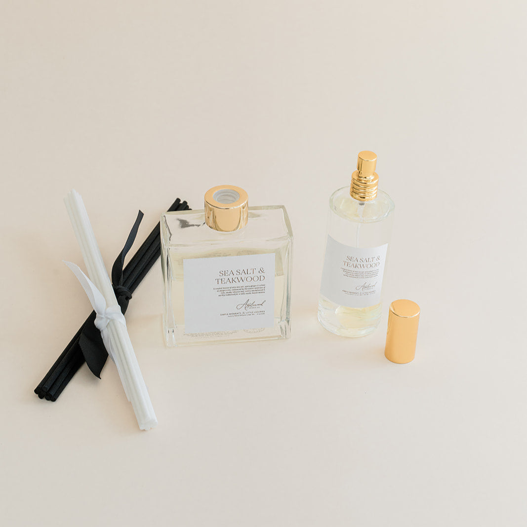 Luxury Flameless reed diffuser and linen spray in glass bottles with gold details, styled on beige background.
