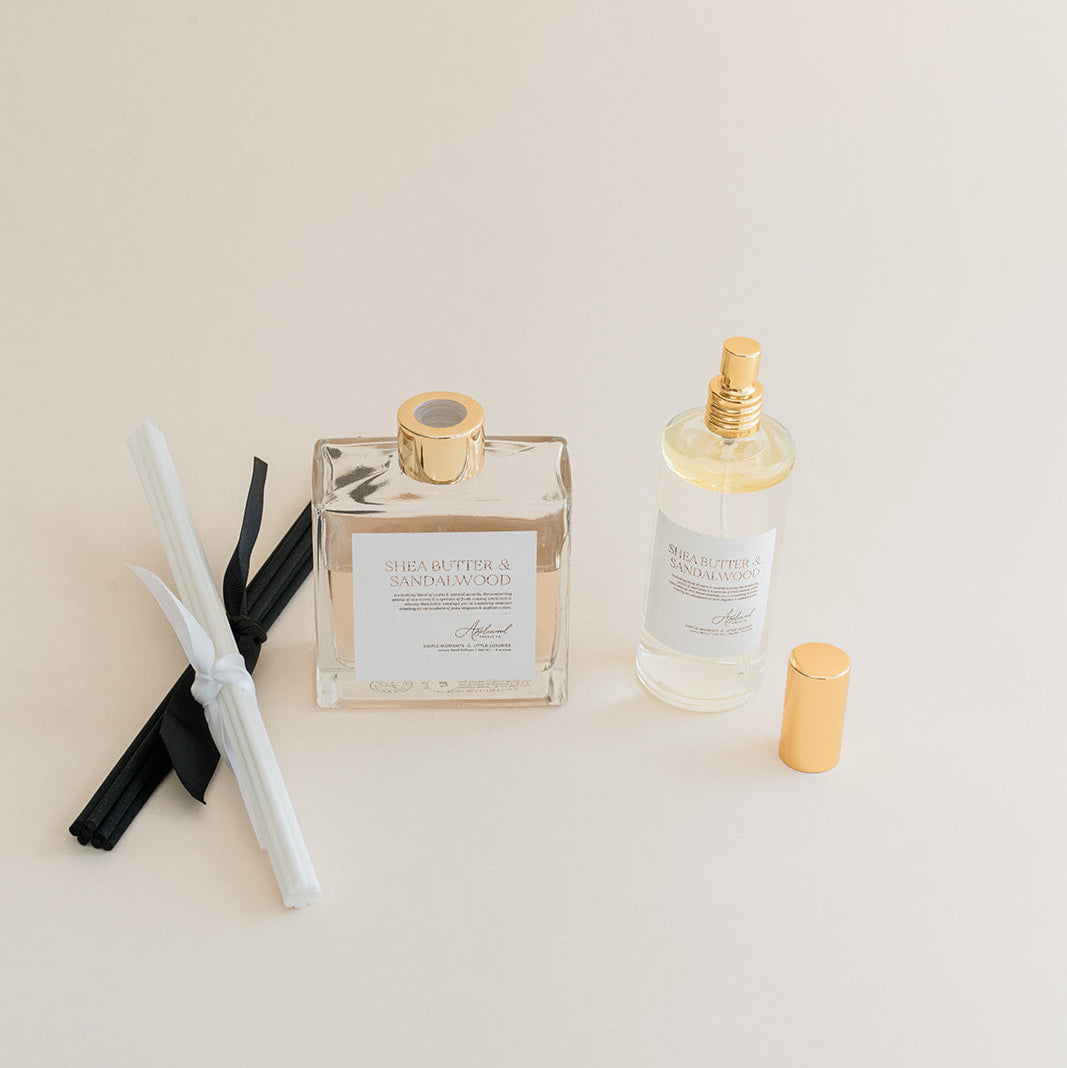 Luxury Flameless reed diffuser and linen spray in glass bottles with gold details, styled on beige background.