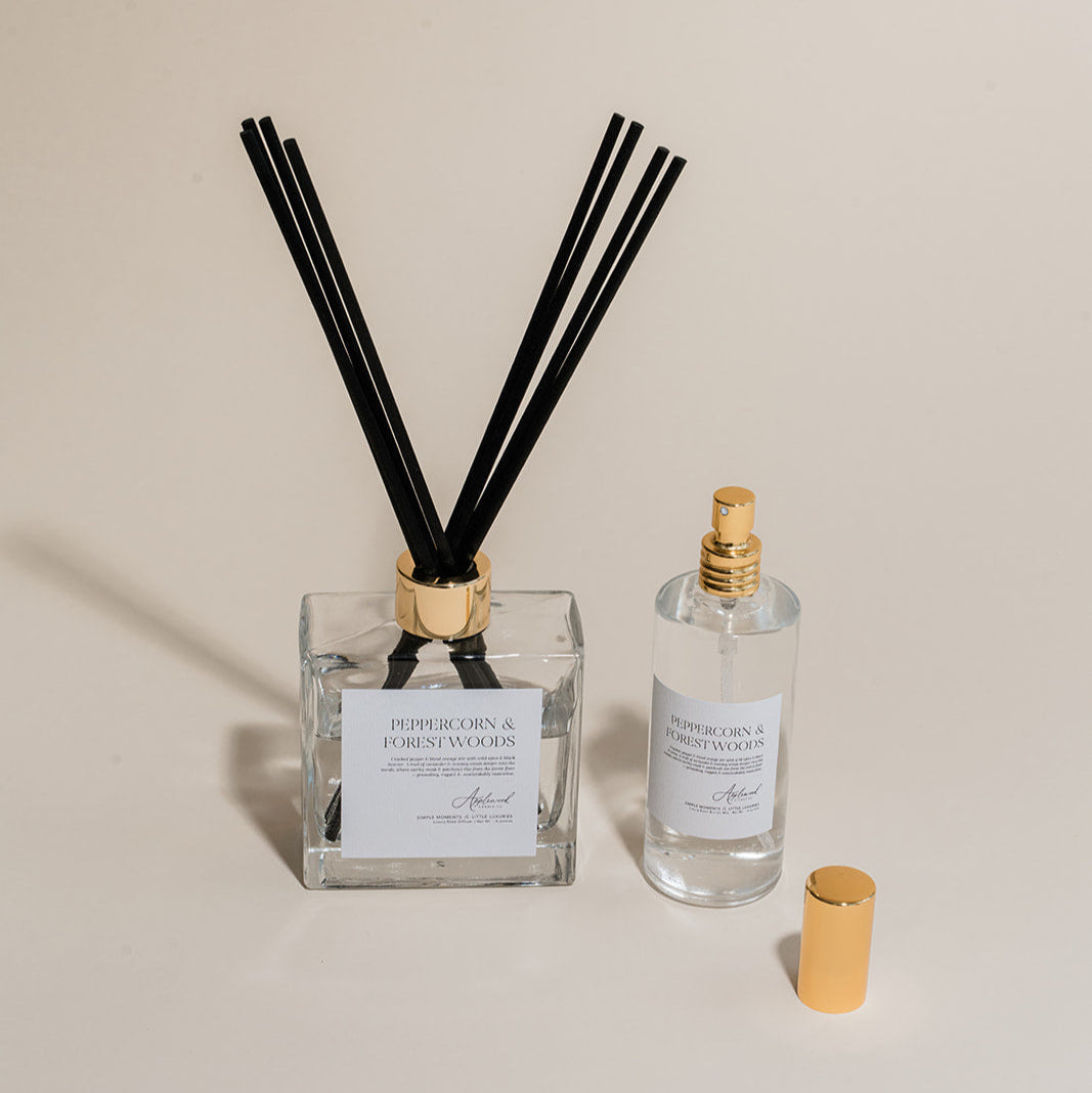 Luxury Flameless reed diffuser and linen spray in glass bottles with gold details, styled on beige backdrop.