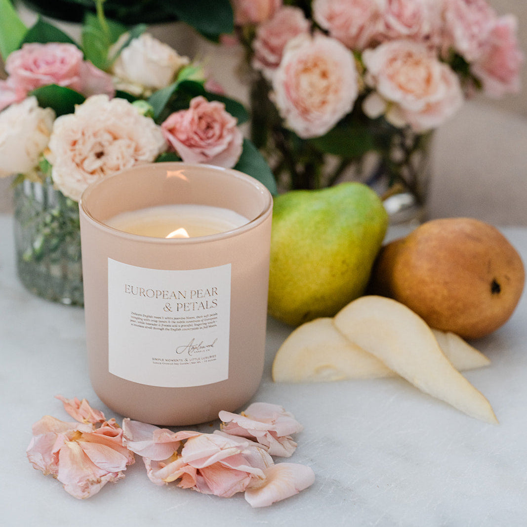 Candle with a floral label surrounded by flowers and pears on a marble surface