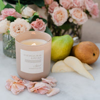 Candle with a floral label surrounded by flowers and pears on a marble surface