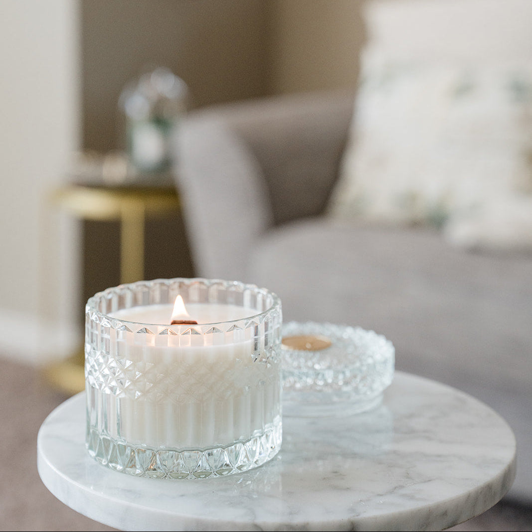 Candle in a textured glass holder on a marble surface with a blurred background