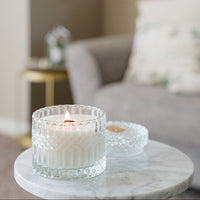Candle in a textured glass holder on a marble surface with a blurred background