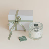 Gift box with a ribbon, glass candle, and card on a beige background