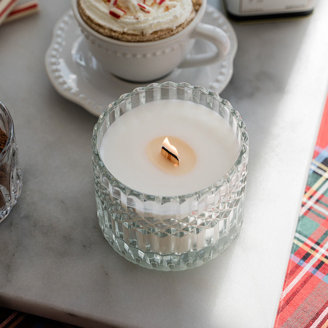 Cup of hot chocolate with whipped cream and a lit candle on a marble surface.
