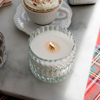 Cup of hot chocolate with whipped cream and a lit candle on a marble surface.