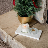 Small potted tree with a red ribbon on a stone ledge next to a candle
