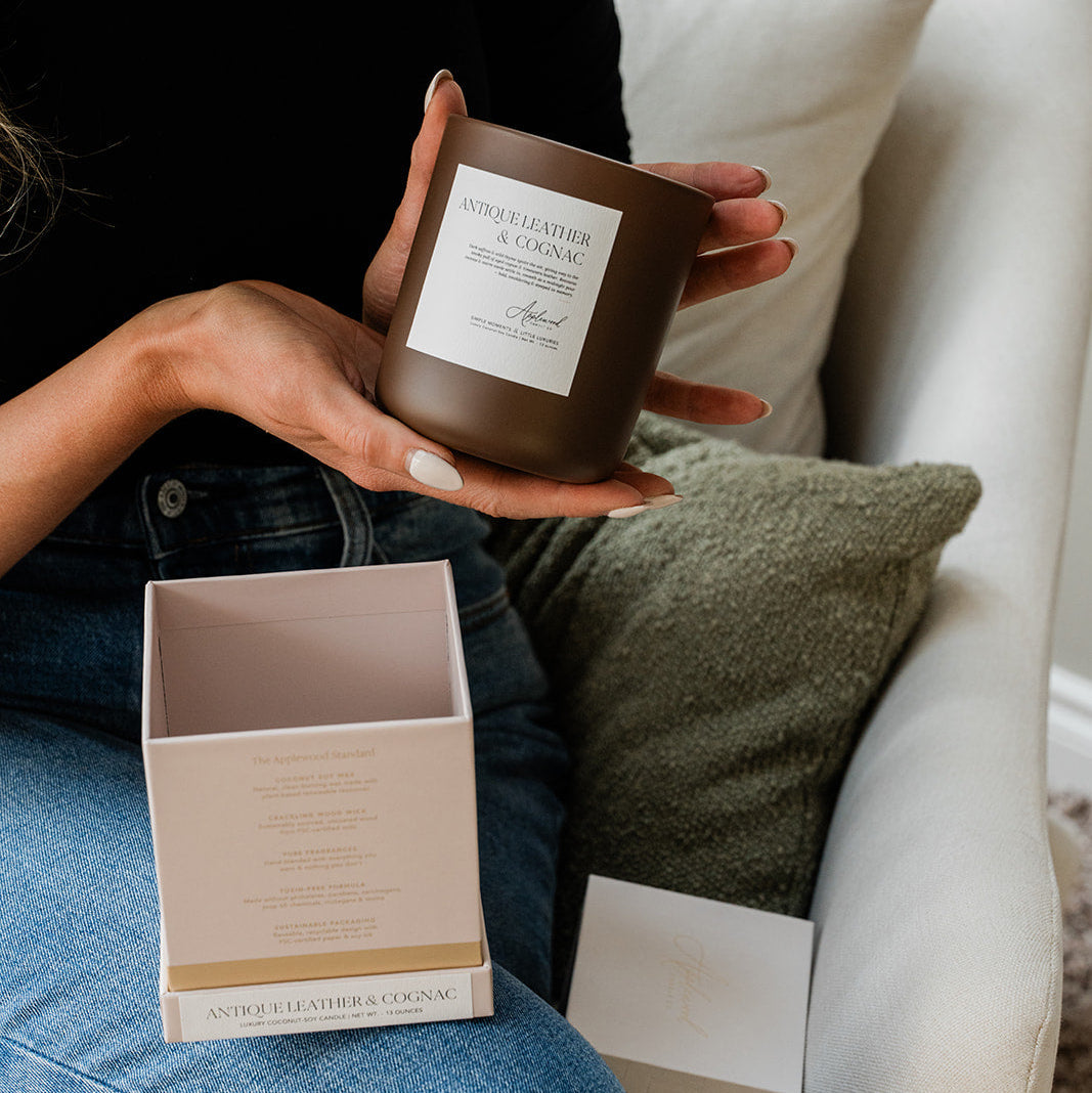 Antique Leather & Cognac candle in brown glass jar being held in hand with opened box beside it.