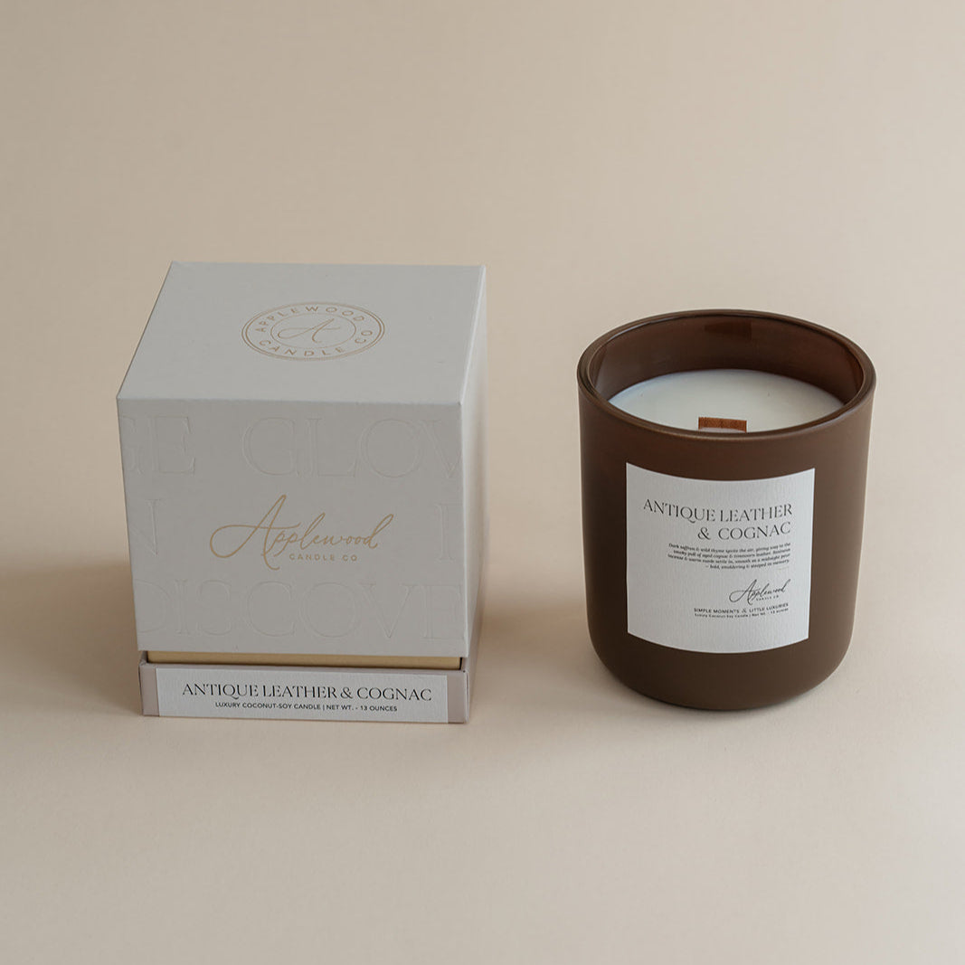 Antique Leather &amp; Cognac candle in brown glass jar with box on beige background.
