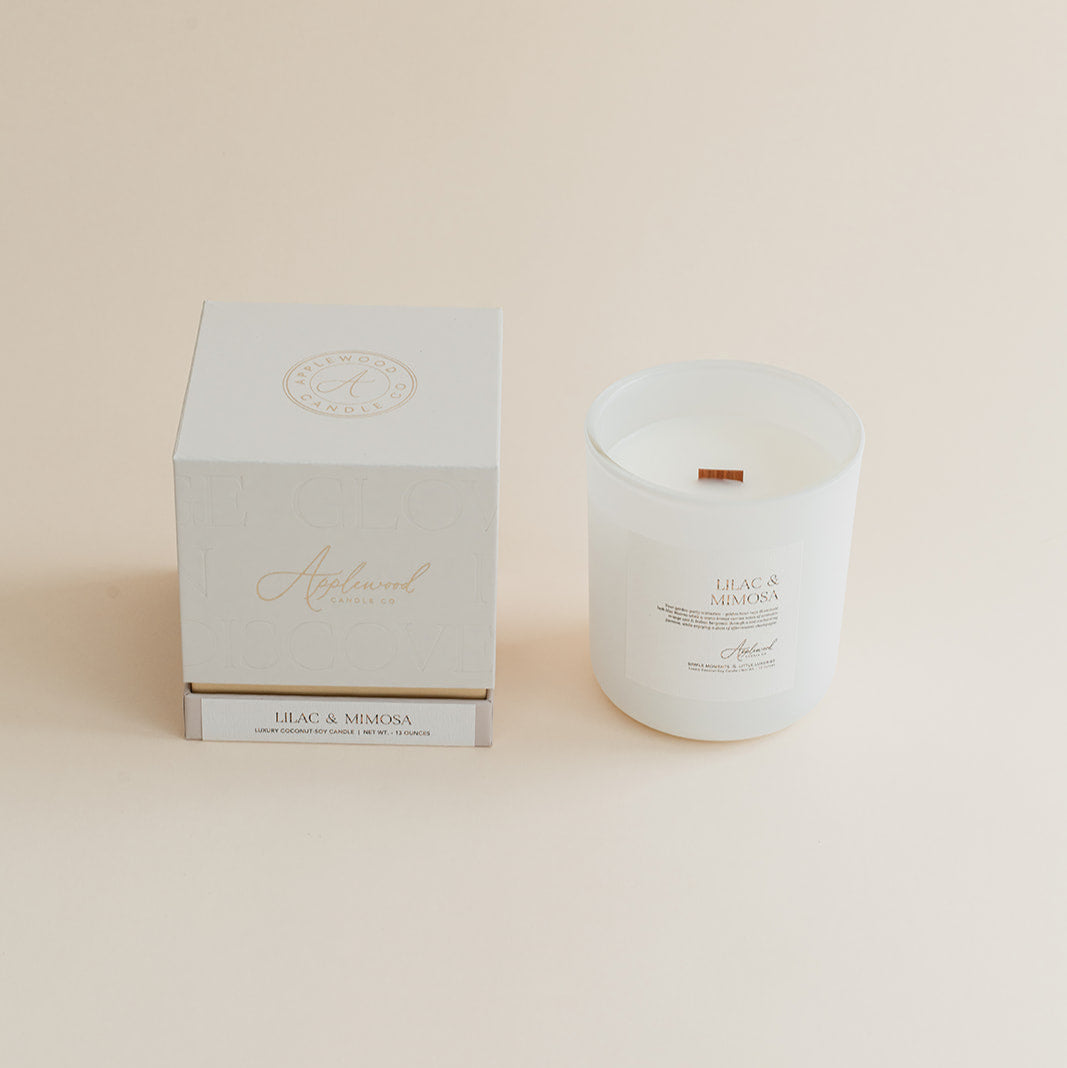 Lilac & Mimosa candle in frosted glass jar with box on beige background.