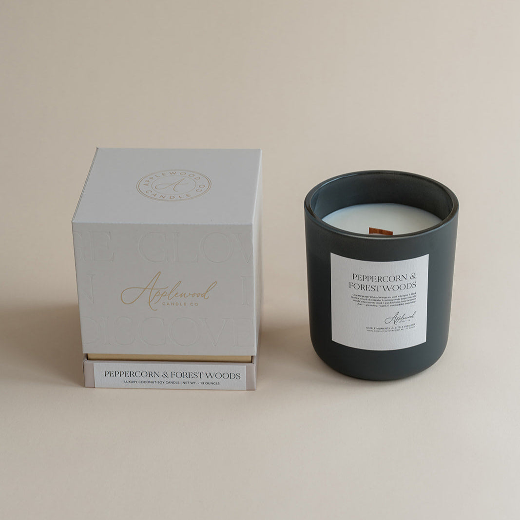 Peppercorn & Forest Woods candle in frosted glass jar with box on beige background.