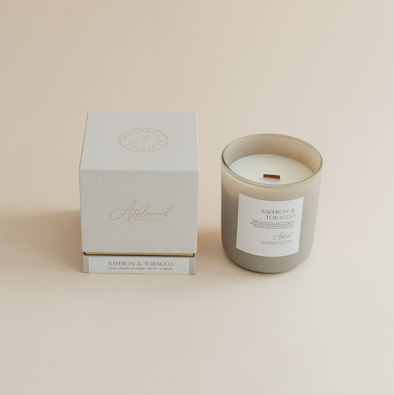 Saffron & Tobacco candle in frosted glass jar with box on beige background.