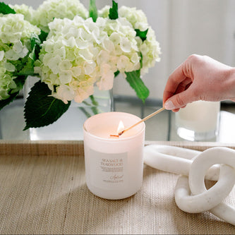 Sea Salt & Teakwood Candle in glass frosted jar being lit.
