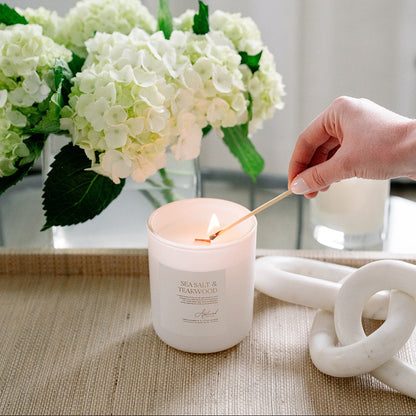 Sea Salt &amp; Teakwood Candle in glass frosted jar being lit.