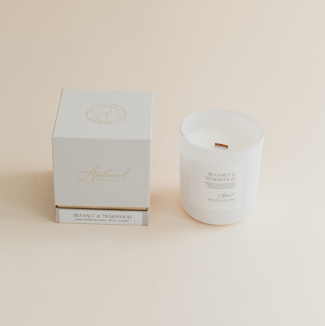 Sea Salt & Teakwood candle in frosted glass jar with box on beige background.
