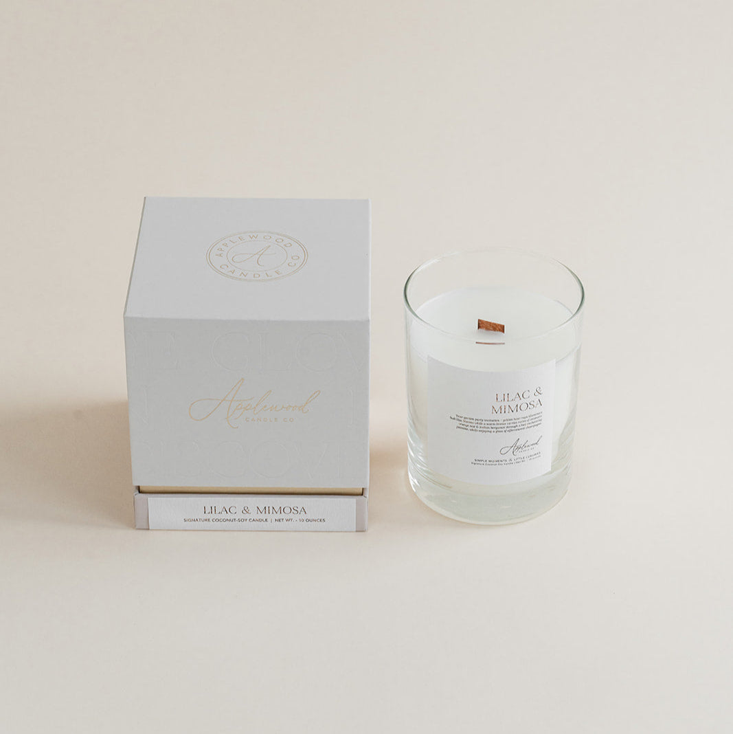 Lilac &amp; Mimosa candle in clear glass jar with box on beige background.