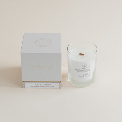 Lilac &amp; Mimosa candle in clear glass jar with box on beige background.