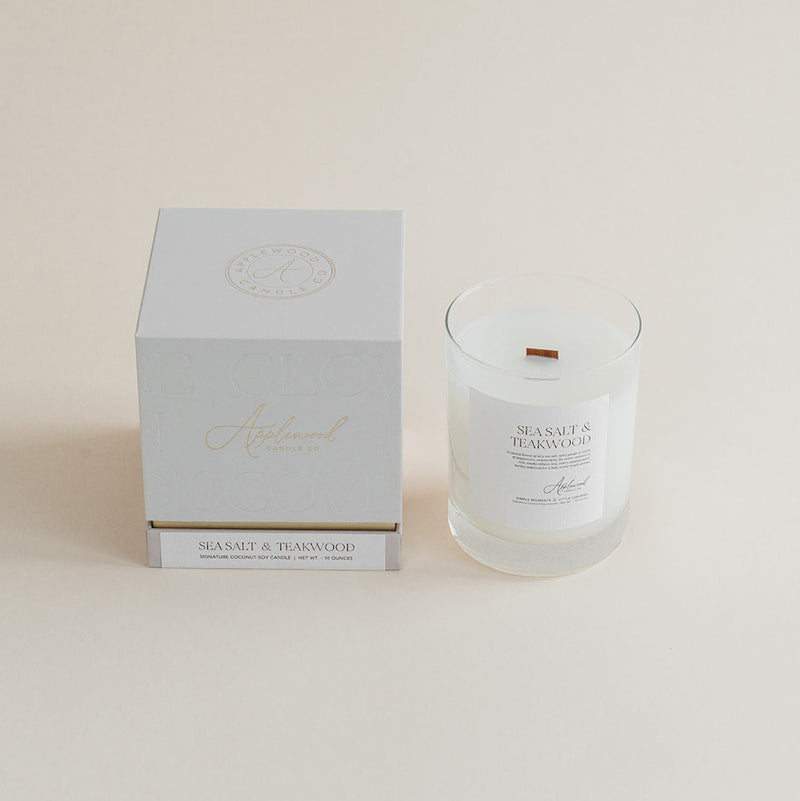 Sea Salt & Teakwood candle in glass jar with box on beige background.
