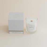 Warm Amber & Santal candle in clear glass jar with box on beige background.