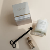 Vetiver & Ember Moss signature candle with box, black wick trimmer and match on a beige background.