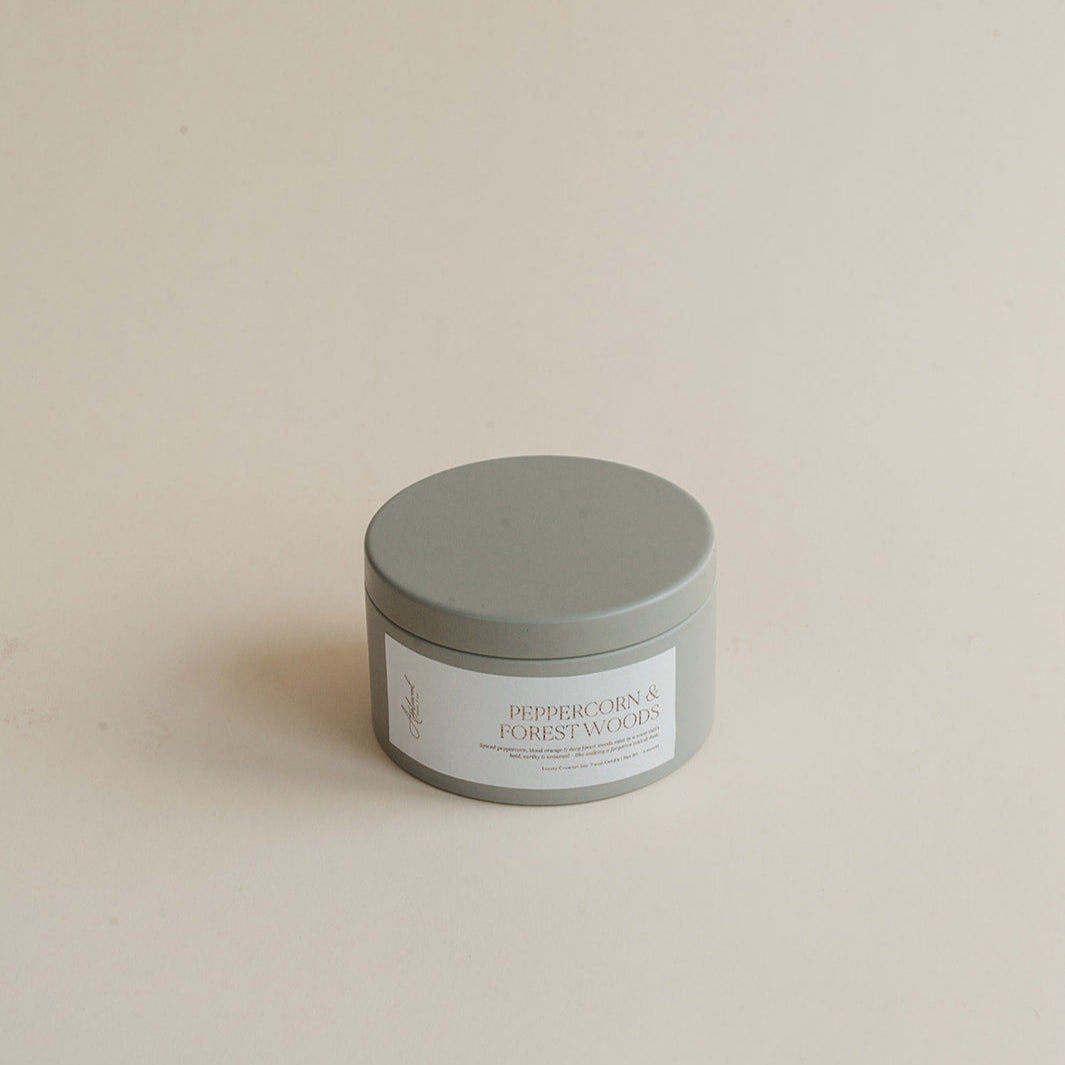 Travel Peppercorn & Forest Woods candle in tin can on beige background.