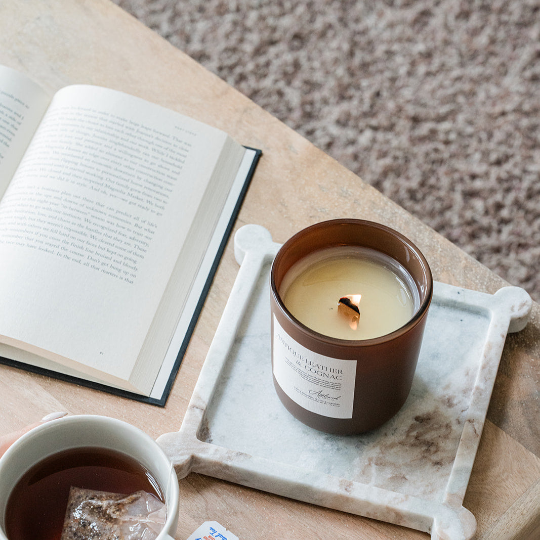 Antique Leather & Cognac candle in brown glass with tea and open book on a cozy background
