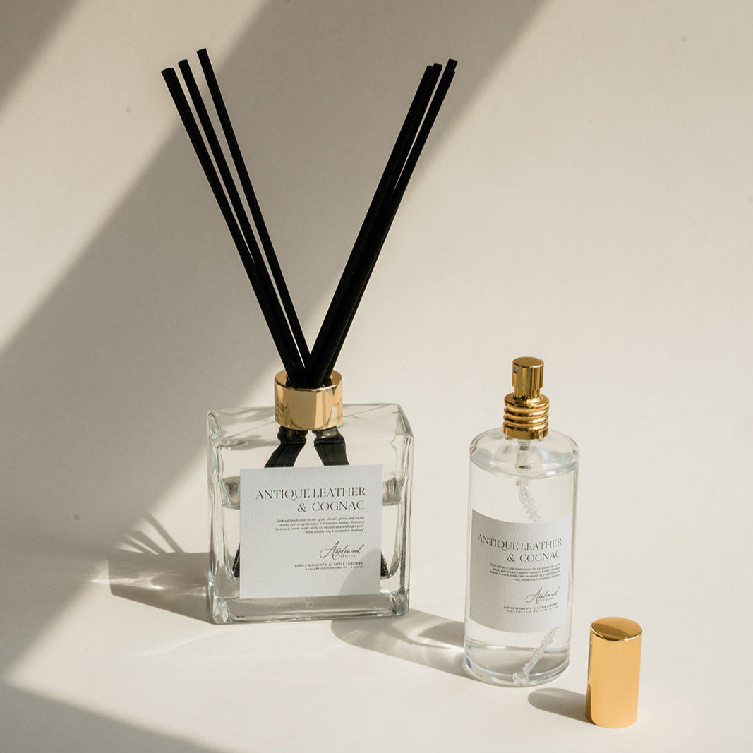 Luxury Flameless reed diffuser and linen mist in glass bottles with gold details, styled on beige backdrop.
