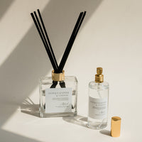Luxury Flameless reed diffuser and linen mist in glass bottles with gold details, styled on beige backdrop.
