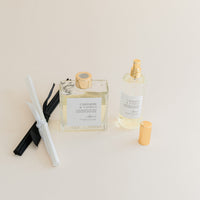 Luxury Flameless reed diffuser and linen spray in glass bottles with gold details, styled on beige backdrop.
