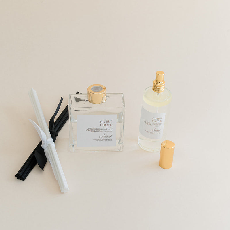 Luxury Flameless reed diffuser and linen spray in glass bottles with gold details, styled on beige backdrop.