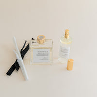 Luxury Flameless reed diffuser and linen spray in glass bottles with gold details, styled on beige backdrop.