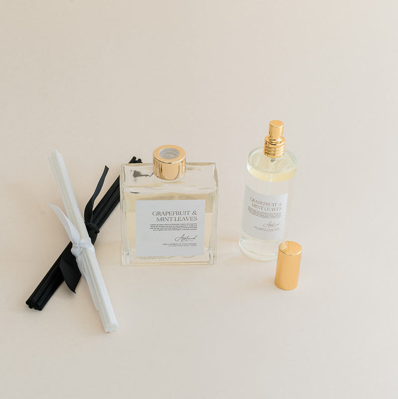 Luxury Flameless reed diffuser and linen spray in glass bottles with gold details, styled on beige backdrop.
