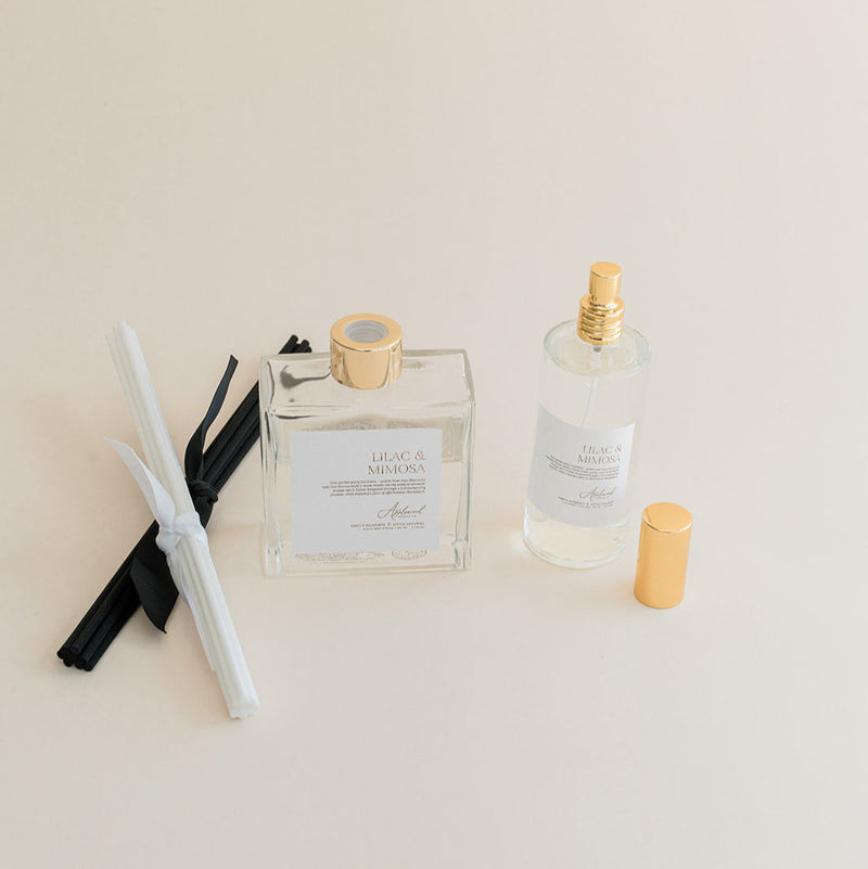 Luxury Flameless reed diffuser and linen spray in glass bottles with gold details, styled on beige backdrop.