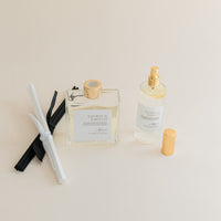 Luxury Flameless reed diffuser and linen spray in glass bottles with gold details, styled on beige backdrop.