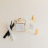Luxury Flameless reed diffuser and linen spray in glass bottles with gold details, styled on beige background.