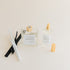 Luxury Flameless reed diffuser and linen spray in glass bottles with gold details, styled on beige backdrop.