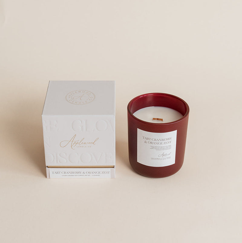 Red candle with a white label next to its box on a beige background