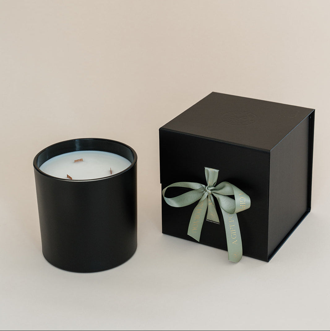 Black candle in a black box with a green ribbon on a beige background