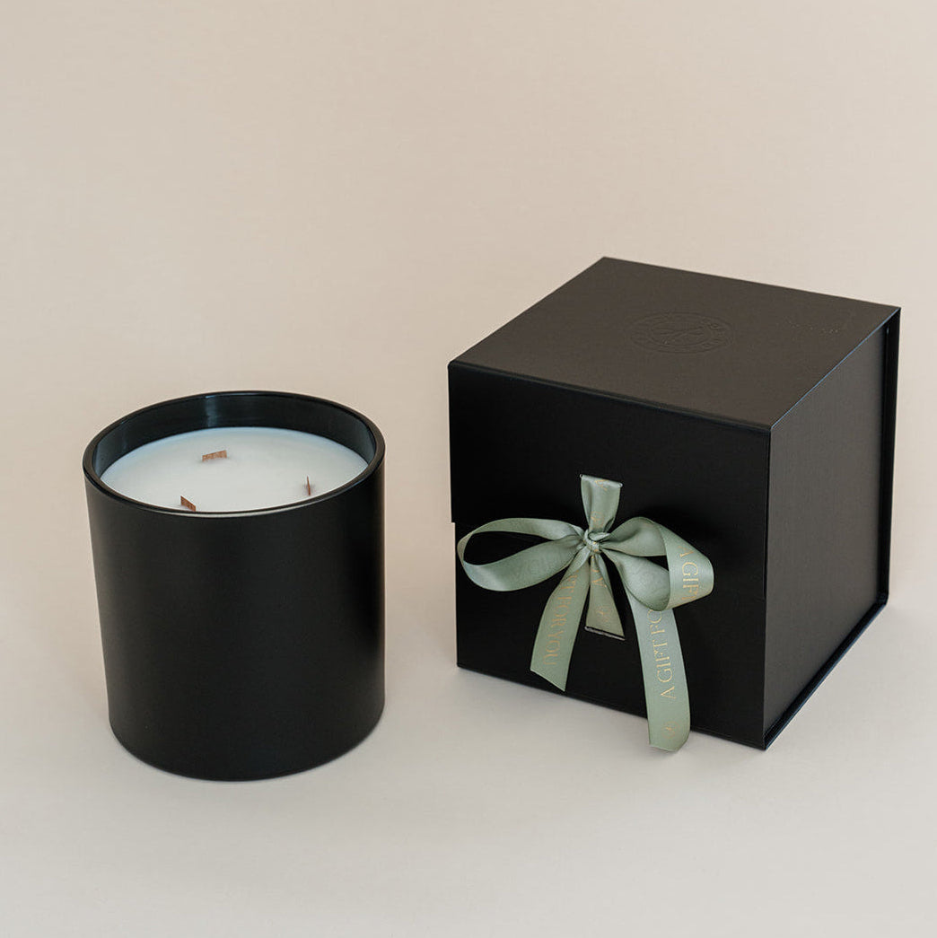 Black candle in a black box with a green ribbon on a beige background
