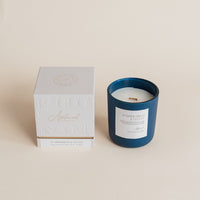 Blue candle with white label next to a white box on a beige background